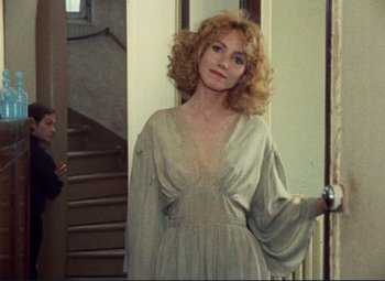 Movie still from “Celine and Julie Go Boating” (1974), directed by Jacques Rivette – A woman in a dress standing in front of a staircase; Medium shot, Over the shoulder angle