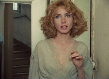Movie still from “Celine and Julie Go Boating” (1974), directed by Jacques Rivette – A woman with blonde curly hair and blue eyes holding a cigarette; Close Up shot, Over the shoulder angle