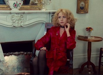 Movie still from “Celine and Julie Go Boating” (1974), directed by Jacques Rivette – A woman sitting in a chair in a room with a fire place; Medium shot, High angle