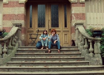 Movie still from “Celine and Julie Go Boating” (1974), directed by Jacques Rivette – Two women sitting on the steps of a building; Wide shot, Low angle