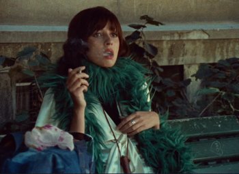 Movie still from “Celine and Julie Go Boating” (1974), directed by Jacques Rivette – A woman in a green boa talking on a cell phone; Medium shot, High angle