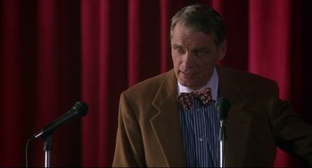 Movie still from “D3: The Mighty Ducks” (1996), directed by Robert Lieberman – A man wearing a suit and bow tie is speaking; Close Up shot, Low angle