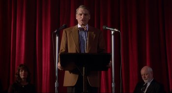Movie still from “D3: The Mighty Ducks” (1996), directed by Robert Lieberman – A man standing at a podium with microphones in front of him; Medium shot, Low angle