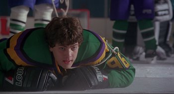 Movie still from “D3: The Mighty Ducks” (1996), directed by Robert Lieberman – A man in a green and yellow hockey uniform laying on the ground; Medium shot, Low angle