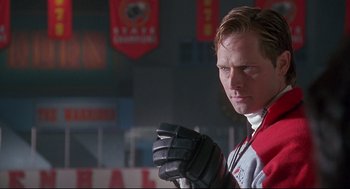 Movie still from “D3: The Mighty Ducks” (1996), directed by Robert Lieberman – A man in a red and white jacket holding a hockey stick; Close Up shot, Low angle