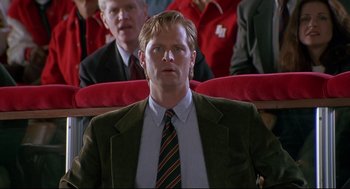 Movie still from “D3: The Mighty Ducks” (1996), directed by Robert Lieberman – A man wearing a suit and tie sitting in front of other men; Close Up shot, Low angle