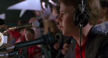 Movie still from “D3: The Mighty Ducks” (1996), directed by Robert Lieberman – A man in a red shirt is talking into a microphone; Close Up shot, Low angle