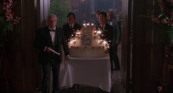 Movie still from “D3: The Mighty Ducks” (1996), directed by Robert Lieberman – A group of men standing around a table with a cake on it; Medium shot, High angle