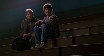 Movie still from “D3: The Mighty Ducks” (1996), directed by Robert Lieberman – Two young men sitting on top of a set of steps; Medium shot, Low angle