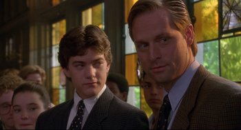 Movie still from “D3: The Mighty Ducks” (1996), directed by Robert Lieberman – Two men in suits and ties standing next to each other in front of stained glass windows; Close Up shot, Over the shoulder angle