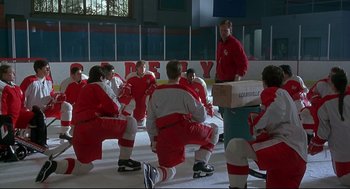 Movie still from “D3: The Mighty Ducks” (1996), directed by Robert Lieberman – A group of men in red and white hockey uniforms sitting on the ice; Wide shot, Over the shoulder angle