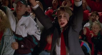 Movie still from “D3: The Mighty Ducks” (1996), directed by Robert Lieberman – A boy in a suit and red neck tie holding his hands in the air; Medium shot, Low angle