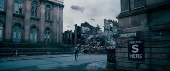 Movie still from “Dad's Army” (2016), directed by Oliver Parker – A man walking down a street near a pile of rubble; Extreme Wide shot, High angle