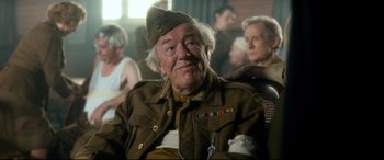 Movie still from “Dad's Army” (2016), directed by Oliver Parker – An older man in a military uniform sitting in a chair; Medium shot, Over the shoulder angle