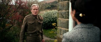 Movie still from “Dad's Army” (2016), directed by Oliver Parker – An older man in a military uniform standing in front of a stone wall; Medium shot, Over the shoulder angle