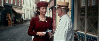 Movie still from “Dad's Army” (2016), directed by Oliver Parker – A woman in a red dress holding a camera and talking to an older man in a hat; Medium shot, Over the shoulder angle