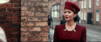 Movie still from “Dad's Army” (2016), directed by Oliver Parker – A woman in a red outfit standing in front of a brick wall; Close Up shot, Over the shoulder angle