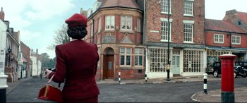 Movie still from “Dad's Army” (2016), directed by Oliver Parker – A woman in a red suit standing in front of a brick building; Wide shot, Low angle
