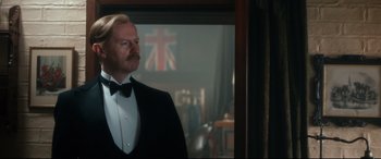 Movie still from “Dad's Army” (2016), directed by Oliver Parker – A man in a tuxedo standing in front of a window; Medium shot, Low angle