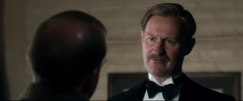 Movie still from “Dad's Army” (2016), directed by Oliver Parker – A person wearing a suit and tie; Close Up shot, Over the shoulder angle