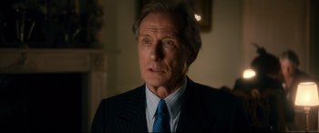 Movie still from “Dad's Army” (2016), directed by Oliver Parker – An older man wearing a suit and tie in a room; Close Up shot, Over the shoulder angle