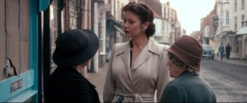 Movie still from “Dad's Army” (2016), directed by Oliver Parker – A woman standing on the sidewalk talking to two other women; Medium shot, Over the shoulder angle