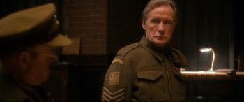 Movie still from “Dad's Army” (2016), directed by Oliver Parker – An older man in a military uniform stands in front of a brick wall; Close Up shot, Over the shoulder angle