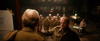 Movie still from “Dad's Army” (2016), directed by Oliver Parker – A group of men in uniform are standing in a room; Medium shot, Over the shoulder angle