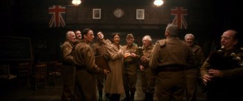 Movie still from “Dad's Army” (2016), directed by Oliver Parker – A group of men and women standing in a room; Medium shot, Low angle