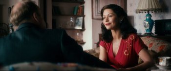 Movie still from “Dad's Army” (2016), directed by Oliver Parker – A woman sitting on a couch in a living room; Medium shot, Over the shoulder angle