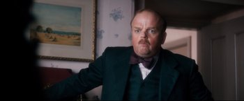 Movie still from “Dad's Army” (2016), directed by Oliver Parker – A man in a suit and bow - tie is making an angry face; Close Up shot, Low angle