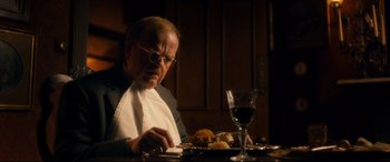 Movie still from “Dad's Army” (2016), directed by Oliver Parker – An older man sitting at a table with a plate of food and a glass of wine in front of him; Medium shot, Low angle