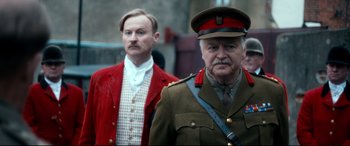 Movie still from “Dad's Army” (2016), directed by Oliver Parker – A man in a military uniform standing next to another man in a red suit; Close Up shot, Over the shoulder angle