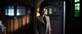 Movie still from “Dad's Army” (2016), directed by Oliver Parker – A woman wearing a coat standing next to a doorway; Medium shot, Low angle