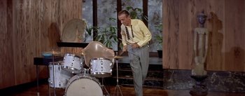 Movie still from “Daddy Long Legs” (1955), directed by Jean Negulesco – A man in a yellow dress shirt and tie playing drums; Medium shot, High angle