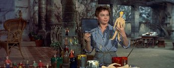 Movie still from “Daddy Long Legs” (1955), directed by Jean Negulesco – A woman is holding a paintbrush while painting a doll; Medium shot, Low angle