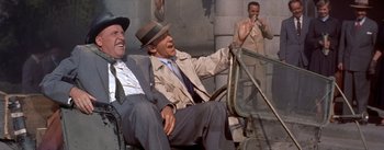 Movie still from “Daddy Long Legs” (1955), directed by Jean Negulesco – Two men sitting next to each other on a bench; Medium shot, Low angle