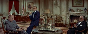 Movie still from “Daddy Long Legs” (1955), directed by Jean Negulesco – A man sitting in a chair holding a piece of food; Medium shot, High angle