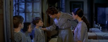 Movie still from “Daddy Long Legs” (1955), directed by Jean Negulesco – An older woman helping a young boy put on a tie; Medium shot, High angle