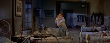 Movie still from “Daddy Long Legs” (1955), directed by Jean Negulesco – A woman holding a child in a room with beds; Wide shot, High angle