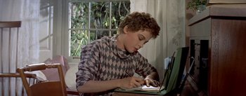 Movie still from “Daddy Long Legs” (1955), directed by Jean Negulesco – A young man is writing on a piece of paper while sitting in front of a window; Medium shot, High angle