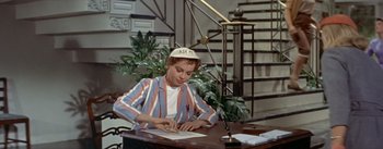 Movie still from “Daddy Long Legs” (1955), directed by Jean Negulesco – A woman sitting at a desk writing on a piece of paper; Medium shot, High angle