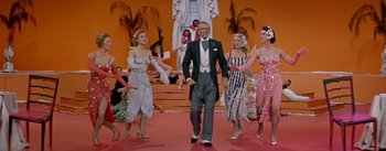 Movie still from “Daddy Long Legs” (1955), directed by Jean Negulesco – A group of people in costumes on a stage; Wide shot, Low angle