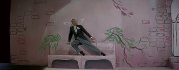 Movie still from “Daddy Long Legs” (1955), directed by Jean Negulesco – A man sitting on top of a wall with wings on it; Wide shot, High angle