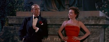 Movie still from “Daddy Long Legs” (1955), directed by Jean Negulesco – A man and a woman standing next to each other in front of a statue; Medium shot, Low angle
