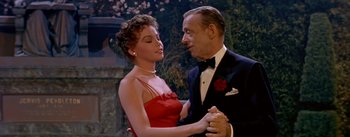 Movie still from “Daddy Long Legs” (1955), directed by Jean Negulesco – An older man and a young woman in a red dress; Medium shot, High angle