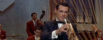 Movie still from “Daddy Long Legs” (1955), directed by Jean Negulesco – A man in a suit and tie holding a trumpet; Close Up shot, Over the shoulder angle