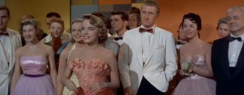 Movie still from “Daddy Long Legs” (1955), directed by Jean Negulesco – A man and a woman in formal wear standing next to each other in front of a crowd; Medium shot, Low angle