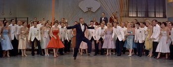 Movie still from “Daddy Long Legs” (1955), directed by Jean Negulesco – A group of people standing in a room with a man in a tuxedo; Wide shot, High angle