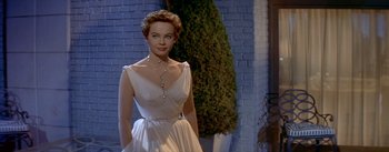 Movie still from “Daddy Long Legs” (1955), directed by Jean Negulesco – A woman in a white dress standing in front of a brick wall; Medium shot, Low angle
